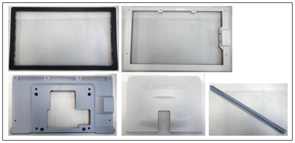 The image displays several plastic or metal parts, likely components for an electronic device or medical equipment, potentially manufactured by GE Healthcare as indicated by the logo on one piece.